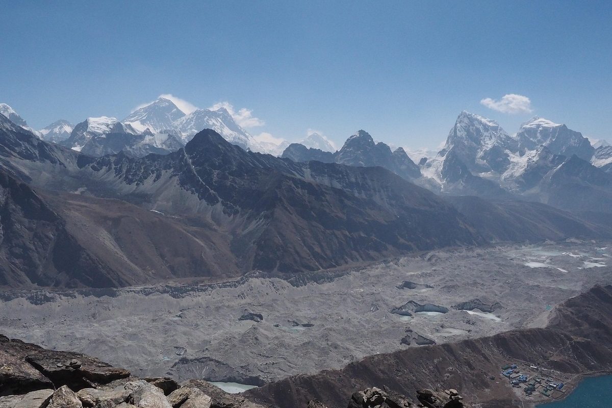 Trekker walking on mountain trail during Everest Base Camp trek with clear blue sky and snow-capped peaks in the background.